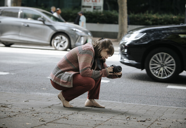 Student with a camera, kneeled down on the street to capture a shot
