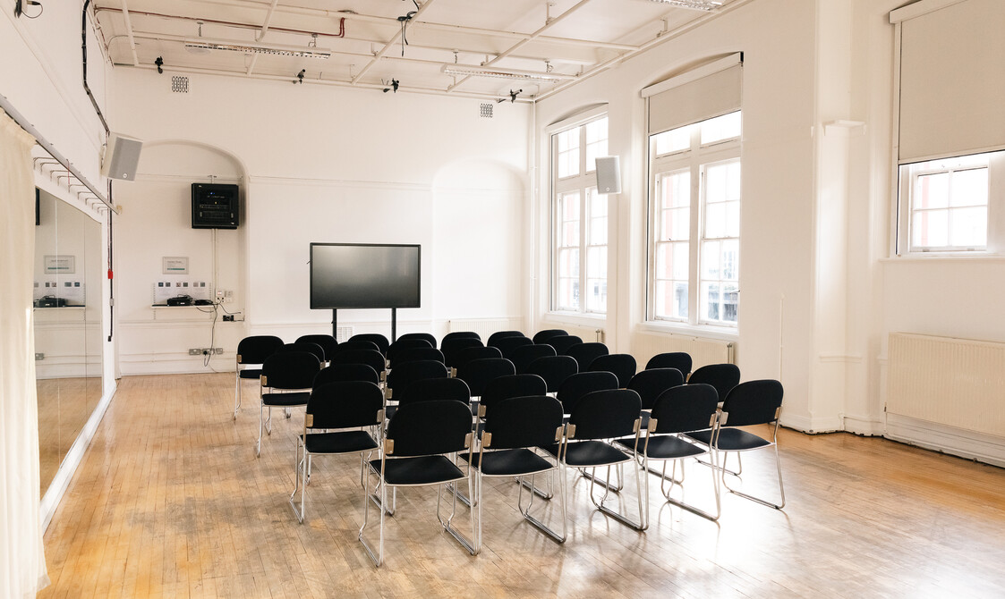 A sunlit room set up with rows of black chairs, facing a large presentation screen.