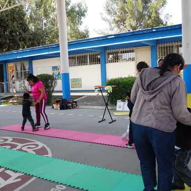 A school yard in which mums and children hold hands facing each other and dance along narrow strips of rubber floor.