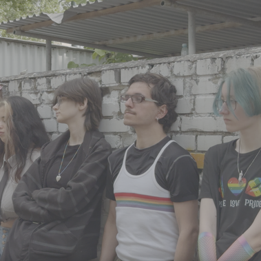 A group of people standing in a row leaning against a long wall, looking ahead into the distance. Some have their eyes closed some open.