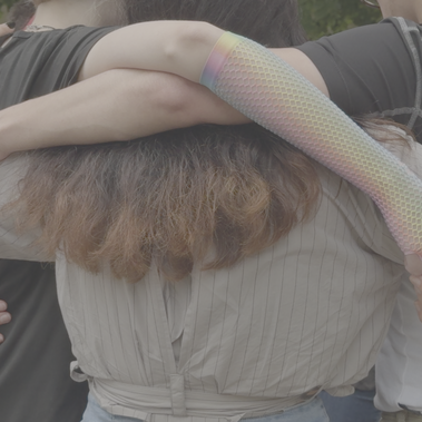 A close group hug with intertwined arms, featuring rainbow-themed accessories, symbolizes solidarity and support.