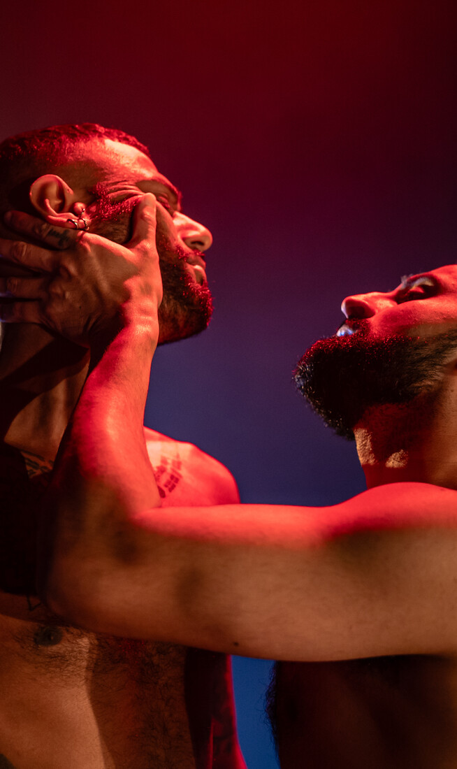 Two men embrace in atmospheric pink and blue lights