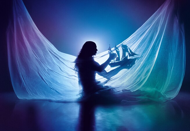 Silhouette of Little M, a Silhouette of Little M, a person with long hair, wearing a draped flowing translucent fabric, holding a model ship with red sails. Backlit to create a dreamy, underwater-like glow, the image evokes a sense of a dreamlike world. with long hair, wearing a draped flowing translucent fabric, holding a model ship with red sails. Backlit to create a dreamy, underwater-like glow, the image evokes a sense of a dreamlike world.