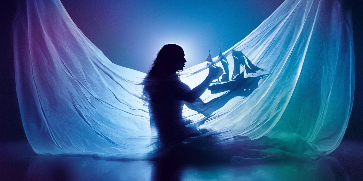 Silhouette of Little M, a Silhouette of Little M, a person with long hair, wearing a draped flowing translucent fabric, holding a model ship with red sails. Backlit to create a dreamy, underwater-like glow, the image evokes a sense of a dreamlike world. with long hair, wearing a draped flowing translucent fabric, holding a model ship with red sails. Backlit to create a dreamy, underwater-like glow, the image evokes a sense of a dreamlike world.