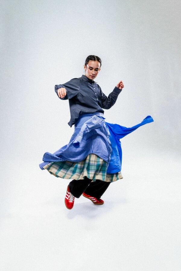 Person wearing a navy shirt and two blue shirts styled as a skirt with red sneakers, caught mid-movement, setting the fabric into motion.