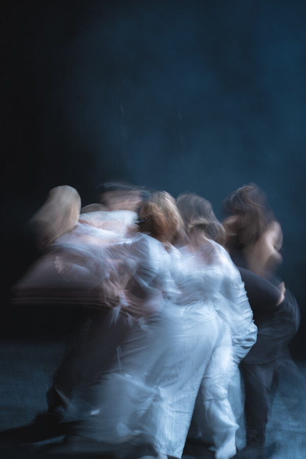 Blurred image of a tightly grouped formation of people, caught mid-motion, dressed in all-white and all-black.