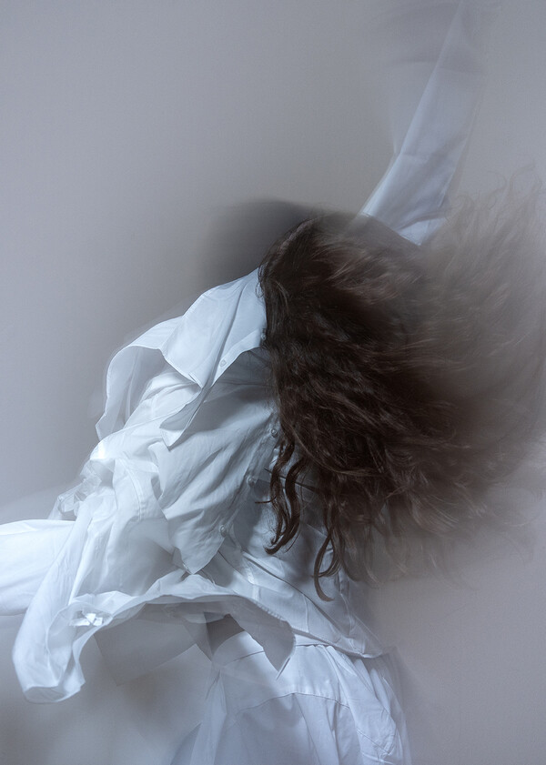 Blurred image of a person captured mid-movement, with their long hair and loose white attire set in flowing motion.