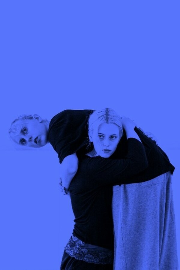 Blue-filtered image of two people wearing black tops, one also in grey tracksuit trousers, with one carrying the other on their shoulder and both holding a forward gaze.