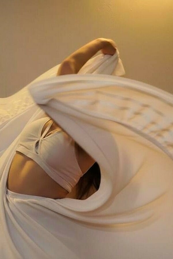 A person wearing a light cream bra and matching long skirt swings the skirt with their arms, causing it to cover their face.