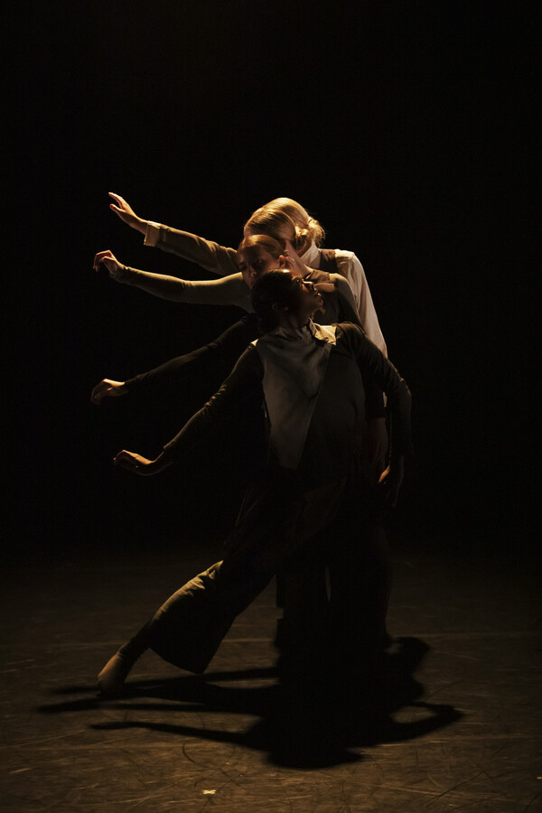 Four people lined up behind one another, each extending their right arm diagonally to the side at gradually increasing heights, creating the appearance of a bird’s wing.