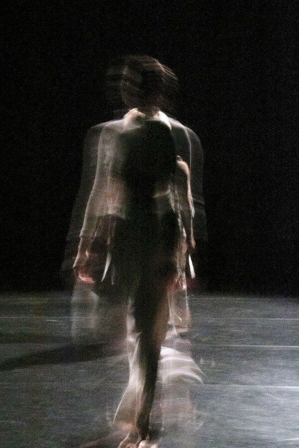 Blurred image of a figure walking, set against a black background.
