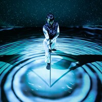 A woman wearing white trousers, a white long-sleeve top, and a navy gilet leans forward onto a long sword, its tip resting at the centre of concentric circles made of blue light and deep shadow. Behind her, a backdrop of scattered light dots against darkness evokes a starry night sky, with a faint green haze resembling northern lights. Her shadow stretches symmetrically to both her left and right, reinforcing the image’s geometric composition. She appears focused and contemplative.