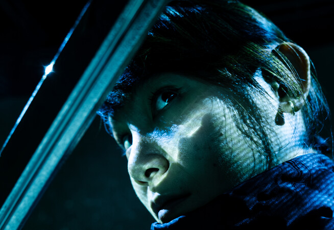 Close-up of a woman gazing from beneath a sword blade that partially covers her face.