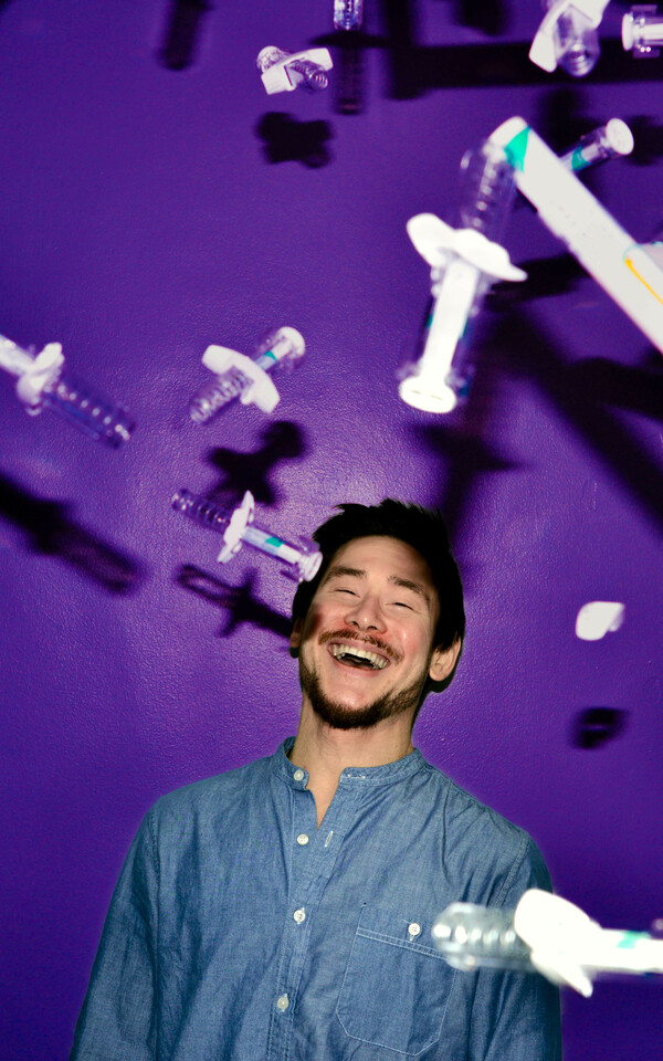 Man shown from the shoulders up laughing against a purple background, surrounded by flying syringes.