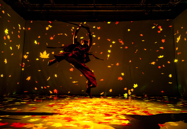 A man suspended mid-jump in a martial arts pose, holding a sword overhead, surrounded by falling leaves.