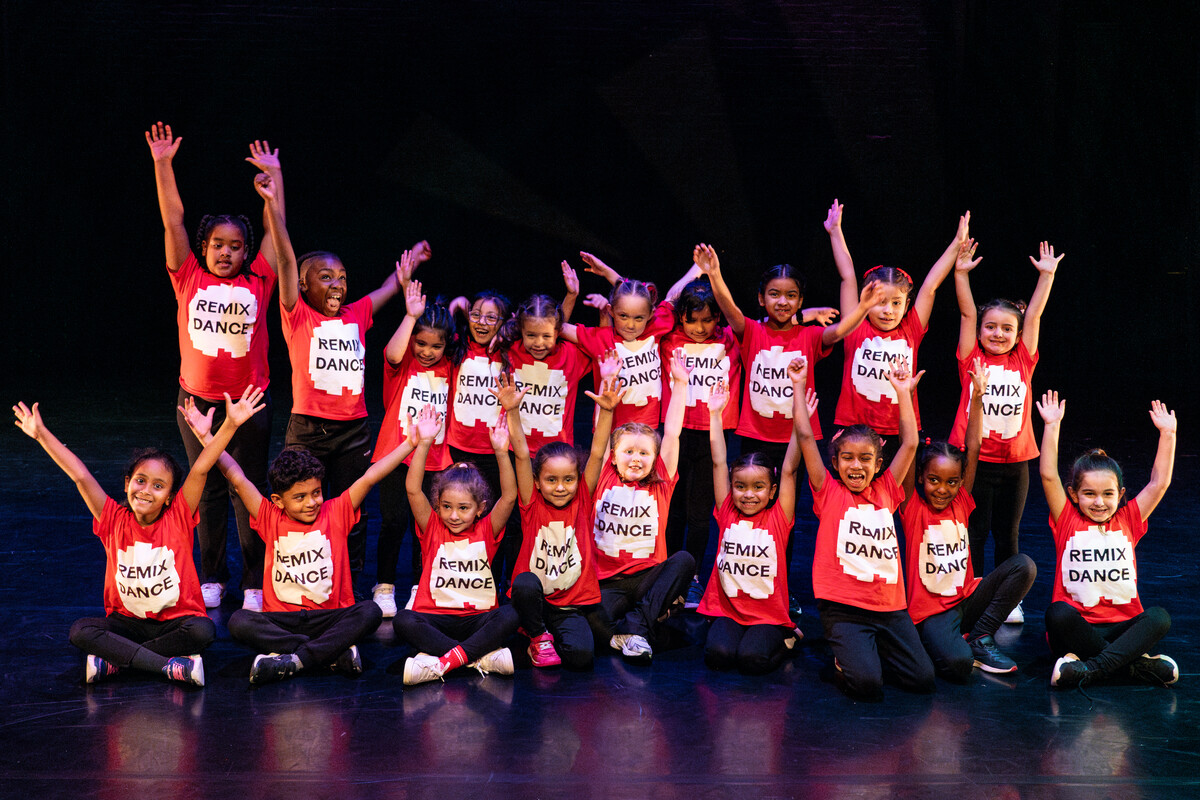 A group of children wearing red T-shirts saying 'RemixDance' raising their arms overhead