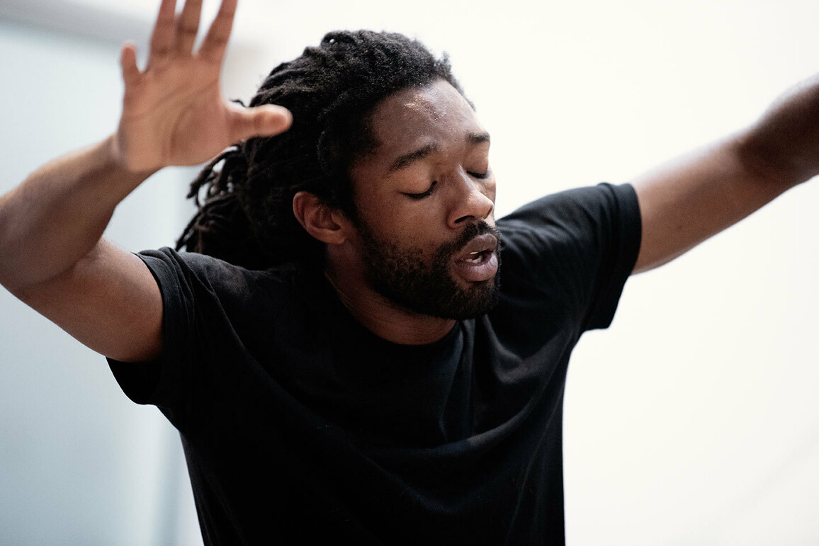 Akeim Toussaint Buck wearing a black t-shirt raising their arms up