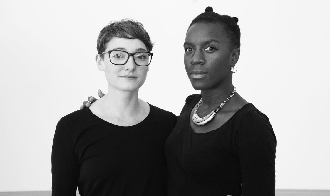 Black and white photo of Phoebe and Nandi facing to camera with their arms around each other.
