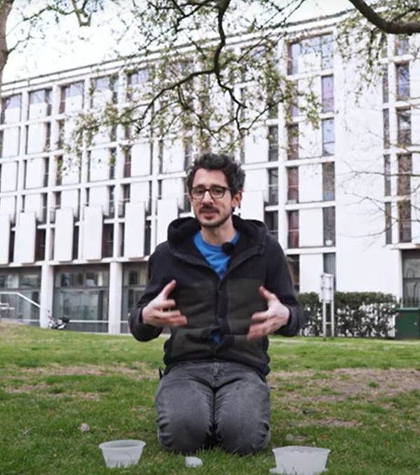 Person sitting on grass with 2 bowls of water. They are holding their hands out in front of them explaining something.