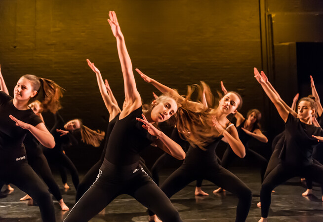 A group of secondary school students on The Place stage wearing black tops and trousers dancing
