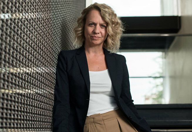 Clare Connor, Chief Executive of The Place is standing in a staircase wearing a white t-shirt and a blazer