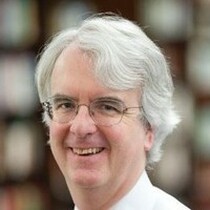 A white man wearing glasses, He has white hair and is wearing a white shirt