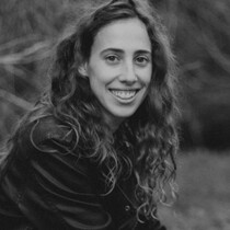 Black and white photo of Sivan in nature. She is looking at the camera smiling. She has long curly hair.