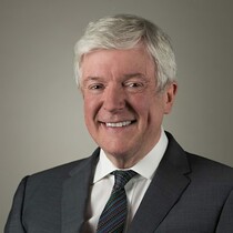 Image of Tony Hall, patron of The Place. Tony is a white man with grey /silver hair. He is wearing a dark grey suit with a white shirt and dark tie.