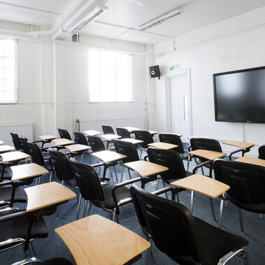 A lecture room is set up with individual chairs with desks facing a screen.