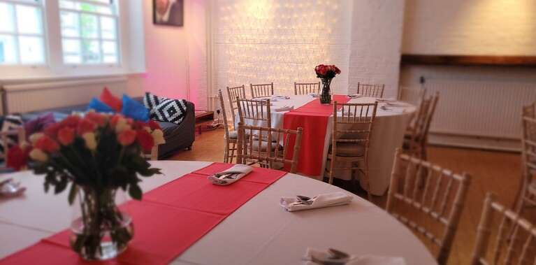 The Place bar dressed with tables and tablecloths and chairs. The tables have white tablecloths and red runner with bouquets of flowers as cetrepieces