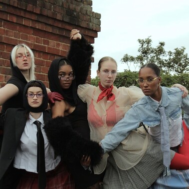 5 dancers pose with limbs intertwined with one another. All wear a mixture of textured and coloured clothing.
