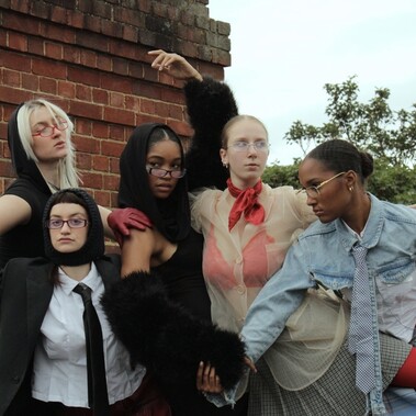 5 dancers pose with limbs intertwined with one another. All wear a mixture of textured and coloured clothing.