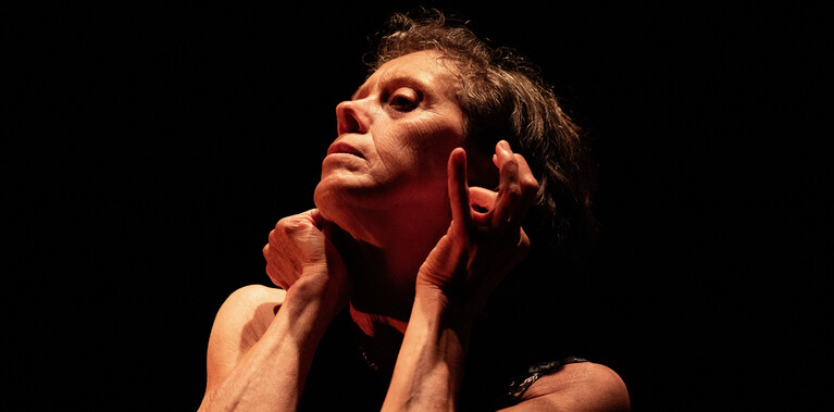 A close up of a woman looking for absent earrings in her ears. Her bare arms show well defined muscles.