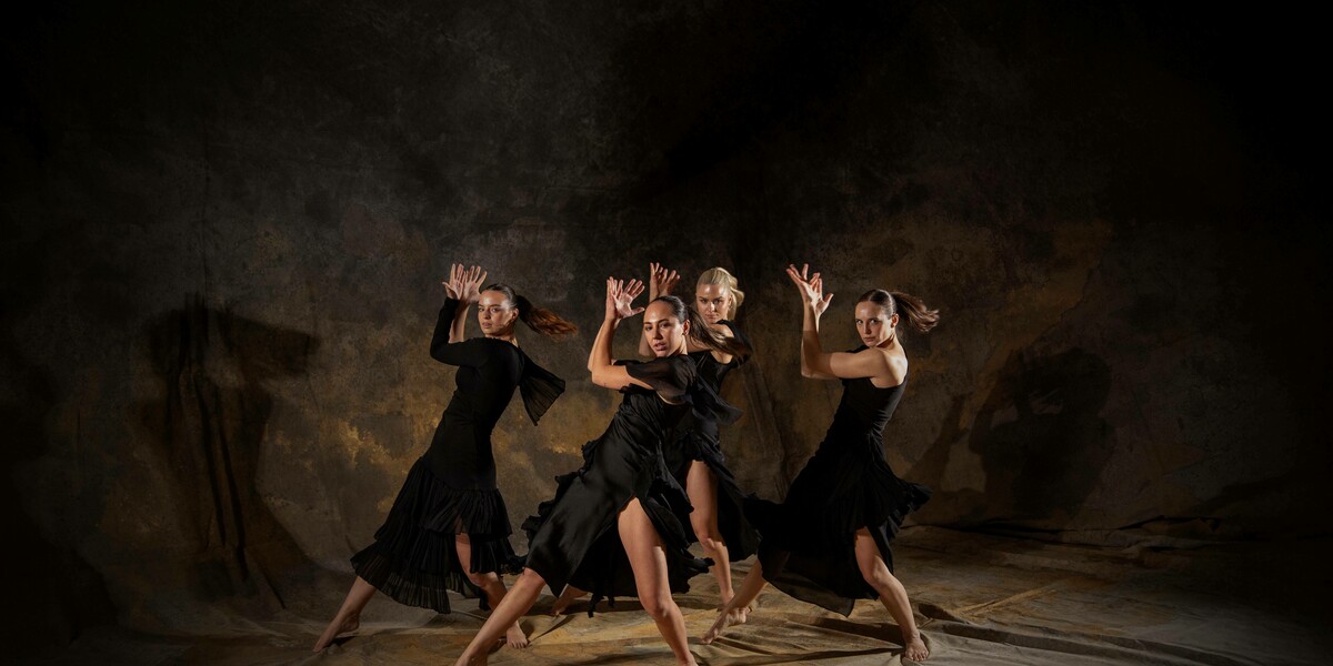 Four dancers in the same dynamic twisted position, hands in an expressive position near their faces. They are against a mottled fabric background.