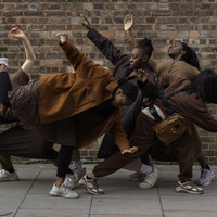 Image of five dancers all in a group huddled together. They make different shapes with their arms and bodies.