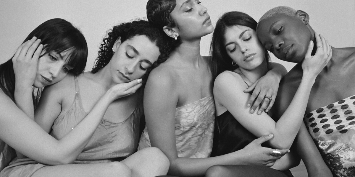 Image of five dancers. They are have their eyes shut and hold on to each other. Their hands caress each other's faces.