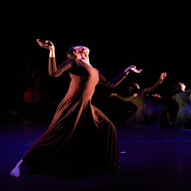 The image shows three female dancers with one at the front, but her face is stretched upwards and two at the back kneeling facing away also looking upwards – all three with their hands outstretched and their faces turned upwards coming out of a harrowing experience.