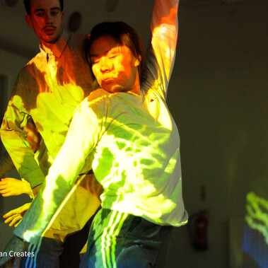 Dancer Yanki Ki Yau and Ivan Merino Gaspar dance. Orange, yellow and green light is projected on them.